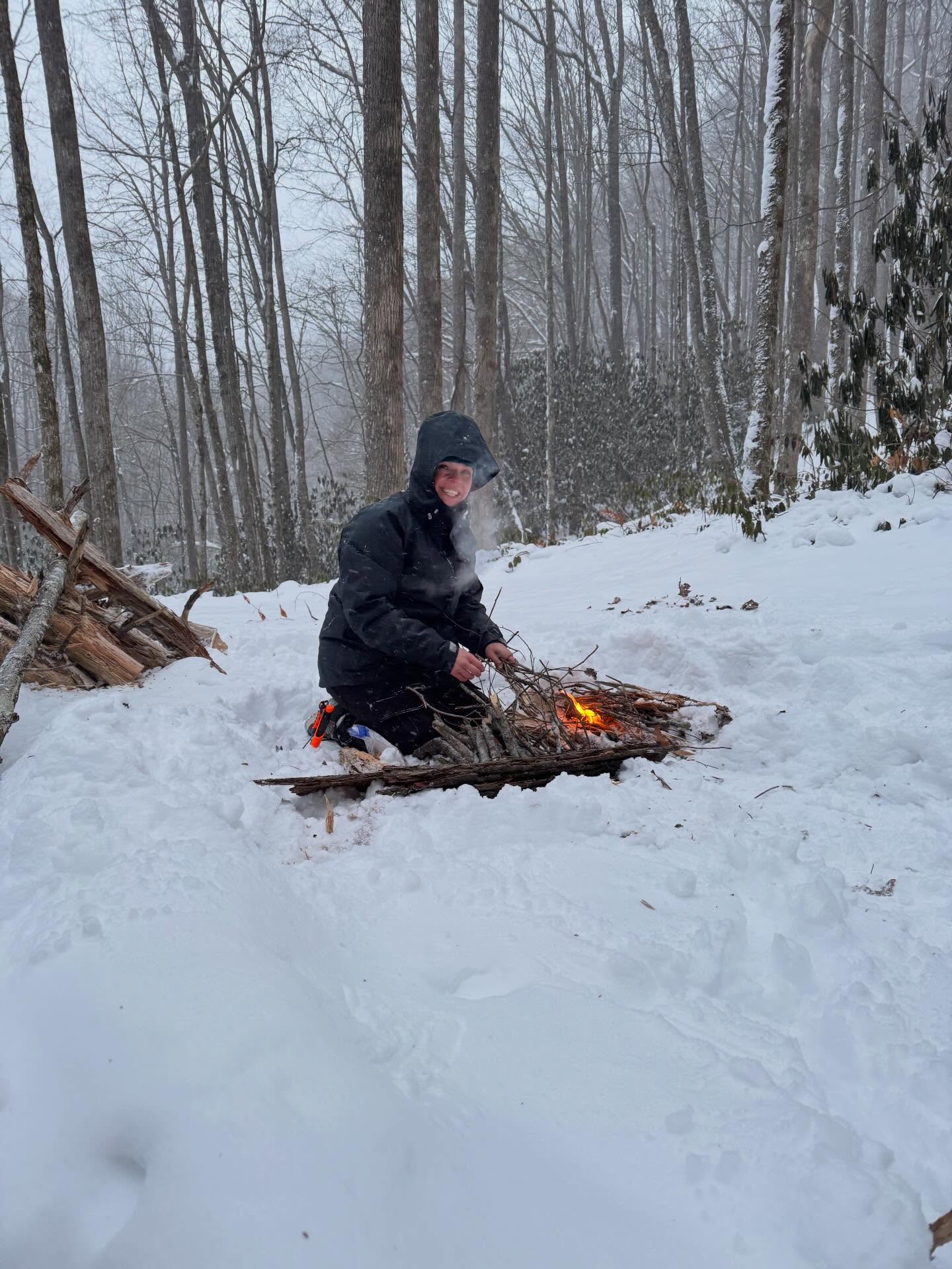 A woman in a black jacket crouching beside a newly made fire